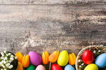 Colorful easter eggs in a basket and tulips on wooden table. Top view. Copyspace