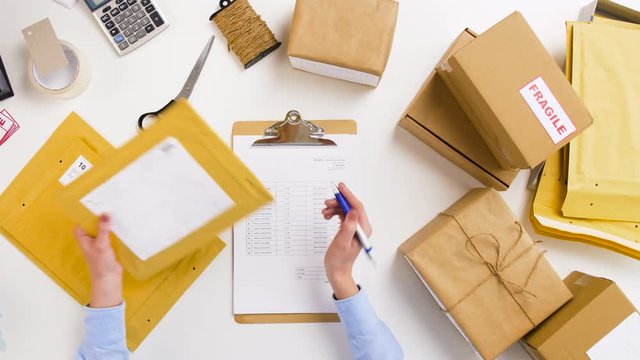 delivery, mail service, people and shipment concept - woman with parcel envelopes, boxes and clipboard working at post office