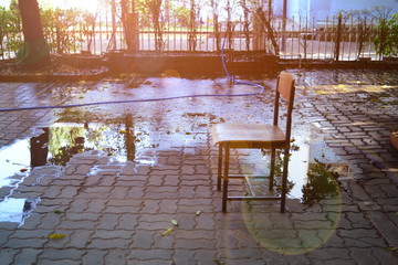 the chair on cement bricks with flare from the morning sun at the garden with water from sprinkler