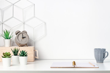 Creative hipster's desk at a white wall. Space for drawing and work. Succulents, a concrete alarm clock, a cup of coffee, an open notebook and a metal graphic board - a toolbox. Copy space for text
