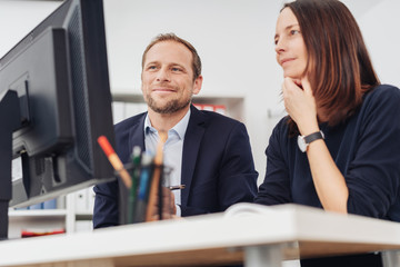 Low angle of two colleagues looking at PC screen