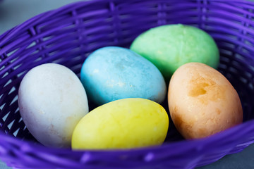 Five multicolored decorative eggs in a purple basket on a gray background. Easter concept.