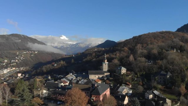 Drone shot over looking the medieval city of Conflans, in the French Alps , focus on the church of the village, in the middle of the mountains, on a sunny day.