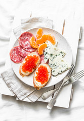 Breakfast in bed - red caviar sandwiches, blue cheese, salami, tangerines on a light background, top view. Flat lay, copy space