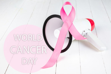 The text world cancer day and a pink ribbon with megaphone on a white wooden table background. The cancer, health, breast, awareness, campaign, disease, help, care, support, hope, illness, survivor