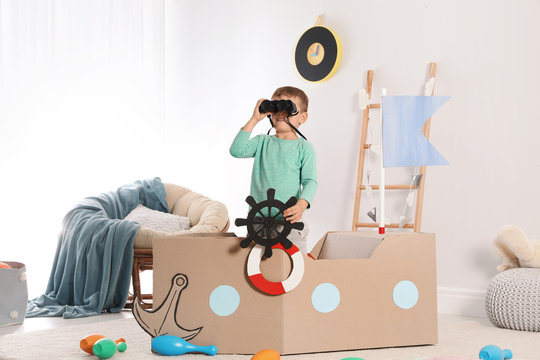 Cute little boy playing with cardboard ship at home