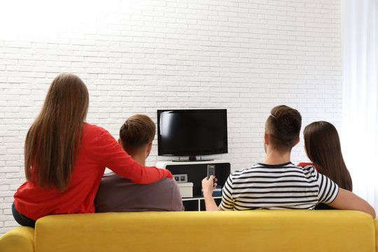 Group of people watching TV together on sofa in living room. Space for text