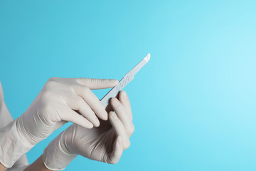 Female doctor holding scalpel on color background, closeup view with space for text. Medical object