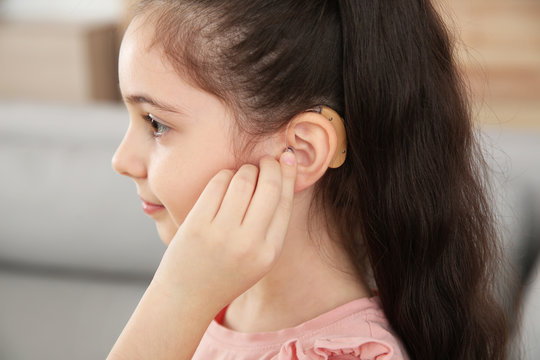 Little girl adjusting hearing aid at home