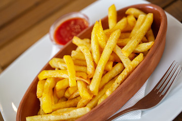 Clay oval plate of french fries on a wooden table