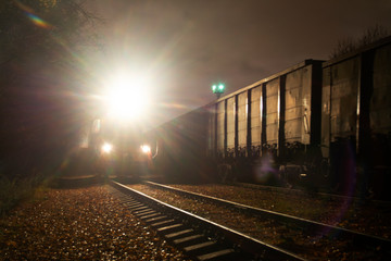 A locomotive with lights on is standing at night on the railway preparing for the departure