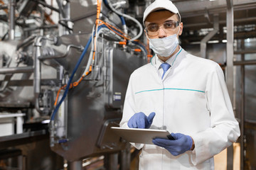 man in a mask and a Bathrobe stands with a tablet in his hands at the dairy Plant