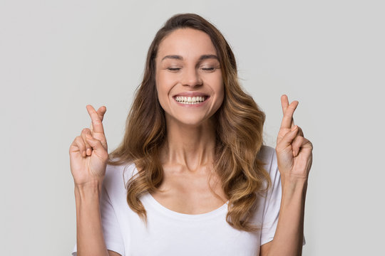 Young Woman Crossing Fingers Wishing For Good Luck Isolated On White Studio Wall, Funny Superstitious Girl Student Hoping Dreams Come True On Blank Light Background, Superstition Beliefs Concept