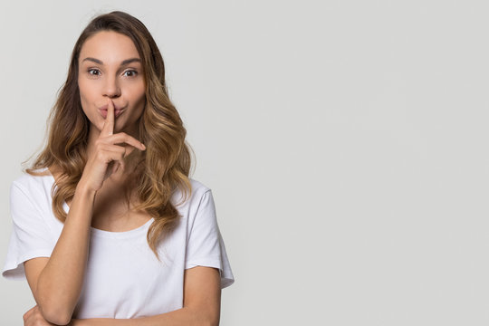 Young woman holding finger on lips mouth to keep it quiet hush standing isolated on white grey blank studio background with copy space, millennial gossip girl showing shh gesture secret in silence