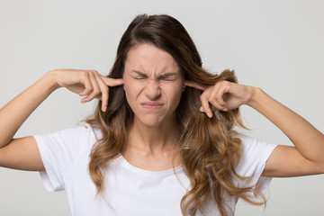 Fototapeta premium Stubborn annoyed woman sticking plug fingers in ears not listening to loud noise sound isolated on white blank studio background, young angry teen refuse hear avoid stress feel ear pain ache concept