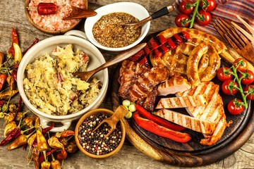 Grilled sausages spiral served on rustic round cutting board with mustard. Homemade barbecue.  Food preparation. Stewed cabbage with meat, mushrooms and sausage.