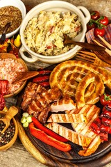 Grilled sausages spiral served on rustic round cutting board with mustard. Homemade barbecue.  Food preparation. Stewed cabbage with meat, mushrooms and sausage.