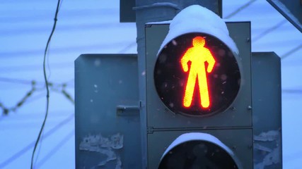 Red traffic control light closeup during snowfall. Slow motion.