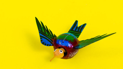 Single traditional wooden handicraft bird miniature toy sideway isolated in saturated yellow background (wide shot)