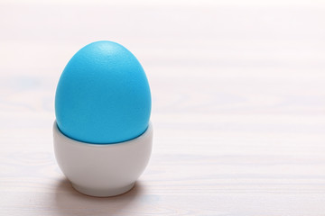 Easter blue egg on a stand on a white table. Copy space