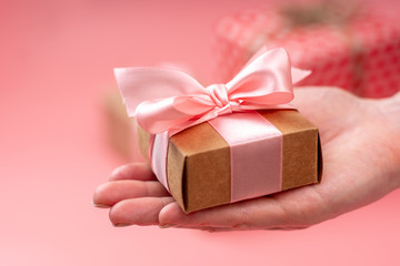Women's hands holding gift box Packed in Kraft paper on pink background. Holiday card for Valentine's and women's day