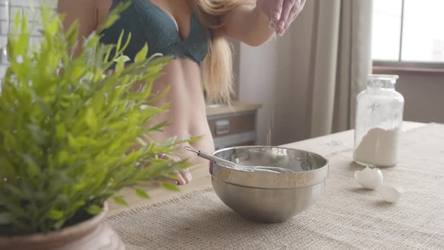 Woman in lingerie takes a pinch of flour and pours into a bowl in the kitchen close up. Unrecognizable girl cooking at home.