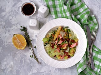 Green salad with avocado, baked salmon and dried tomatoes in a white plate on a gray concrete background. Top view.