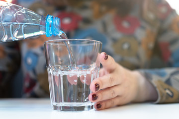 Woman pouring a cold water in a transparent glass in her hand.