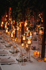 Hindu wedding reception dinner. Tables served with greenery, shiny candles and rose gold decor stands in the restaurant