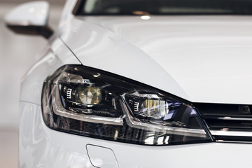 Closeup headlights of a modern white color car. Detail on the front light of a car. Modern and expensive car concept. The car is in the showroom