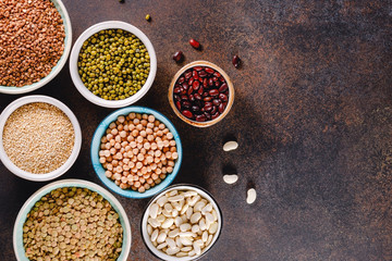 Top view on bowls with various grains on a textured dark background.