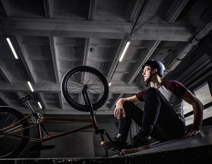 Fototapeta na wymiar Young Bmx rider relaxing after practicing tricks with his bike in a skatepark indoors