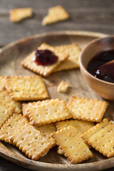 Crackers with cherry jam on a wooden plate on a wooden background. Rustic style