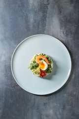 Vegetarian sandwich with chopped avocado, sun dried tomatoes, egg, shrimps, cream cheese served on ceramic plate over blue texture background. Flat lay, space