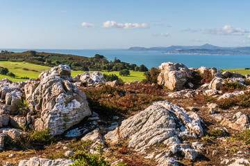 Rocky Irish hill top with limestone rocks leading towards the sea. Amazing view from Howth Head, County Dublin, Ireland on a beautiful blue sky summer day. Colourful landscape.