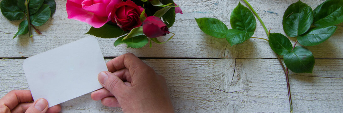 Top view of female decorator holding a  card, arranging roses on the wooden table, Concepts - fiorist, occupation, hobby, small business