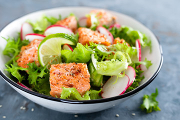 Healthy lunch salad with baked salmon fish, fresh radish, lettuce and lime