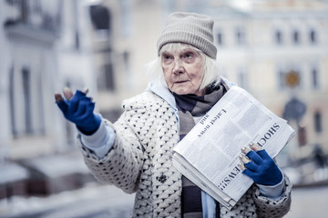 Unhappy aged woman selling newspapers to people