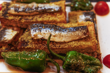 Lisbon, Portugal traditional sardines served food. Close up top view of grilled sardines on toasted bread with olive oil green peppers and tomatoes garnish.