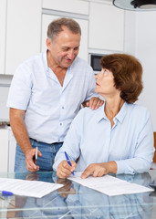 Obraz premium Mature couple at table in home kitchen, woman filling up documents