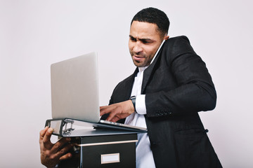 Portrait astonished oficce worker holding folders, laptop talking on phone on white background. Stylish businessman, building career, smart manager, modern work, misunderstanding
