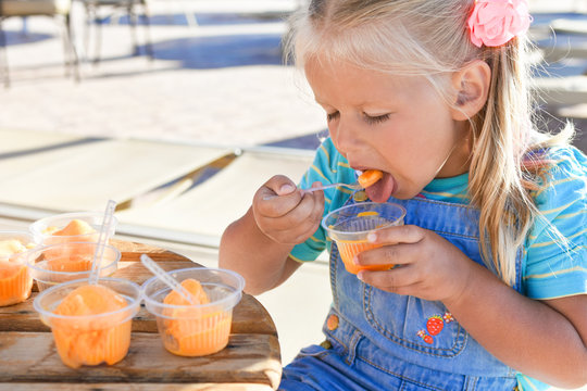 Little girl eating a lot of orange ice cream in a street cafe