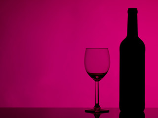 Wine glass and bottle on glossy black glass. Colorful background