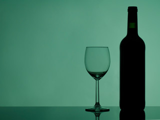Wine glass and bottle on glossy black glass. Colorful background