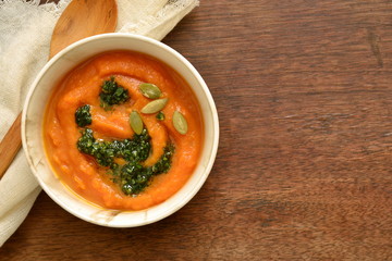 Pumpkin and carrot cream soup with cilantro sauce, seeds, top view, copy space