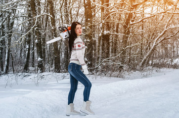 Woman in a sweater and jeans holds a chainsaw on his shoulder, goes in a snowy forest. Job search, sawing wood, employment, deforestation.