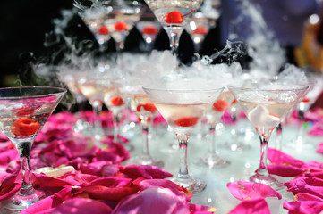 A slide of champagne with dry ice and smoke at the solemn event. Pyramid of glasses with alcohol and cherries.