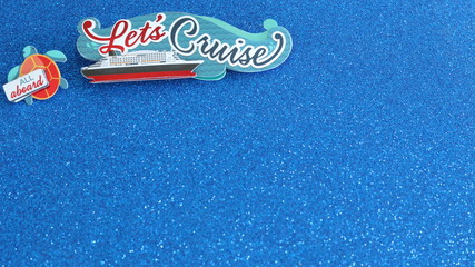 Lets cruise written on a banner with a cruise ship at sea written on a button and all aboard written on a turtle all laying flat on a glittered blue background with writing space