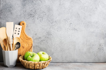 Kitchen shelf. Gray concrete wall kitchen tools for cooking, wicker basket with green apples, cutting board. Horizontal, copy space..