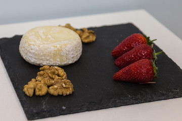 Tomino Cheese on Black Tablecloth decorated with Red Strawberries and Walnuts